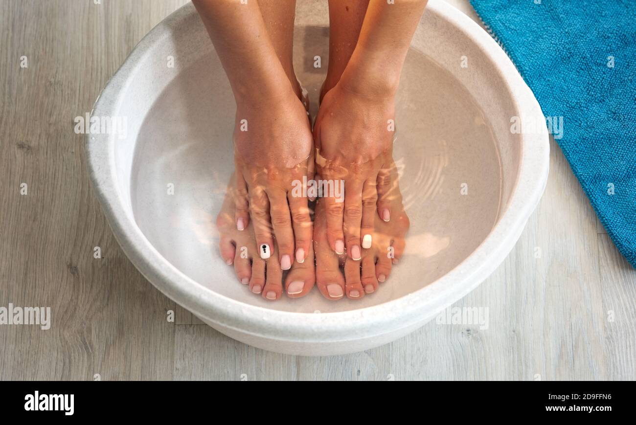 Une femme a mis les mains et les pieds dans le bain avec de l'eau chaude et du bicarbonate de soude à la maison. Bain maison pour les pieds secs Banque D'Images