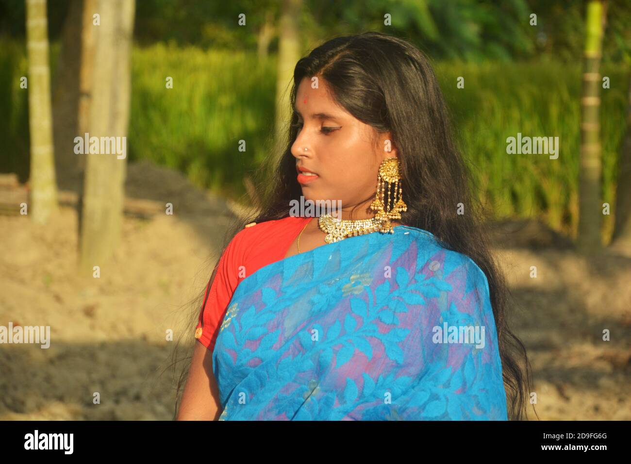 Gros plan d'une jeune fille bengali indienne, portant un sari bleu avec des cheveux longs et une pointe de nez dorée, des boucles d'oreilles, un collier dans un champ labouré, un foyer sélectif Banque D'Images