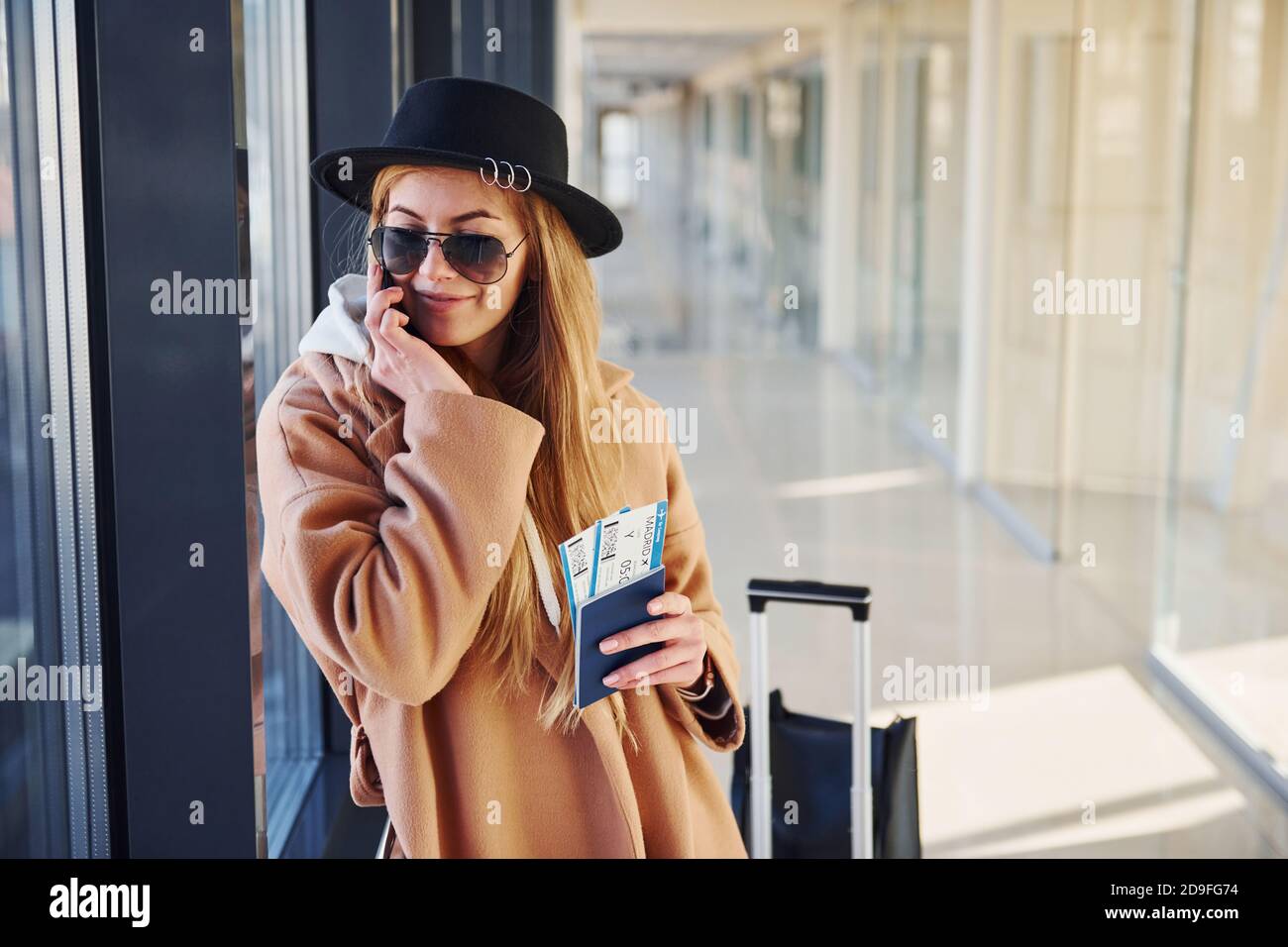 Jeune femme en lunettes de soleil, vêtements chauds et chapeau debout à  l'intérieur de l'aéroport avec téléphone et billets dans les mains Photo  Stock - Alamy