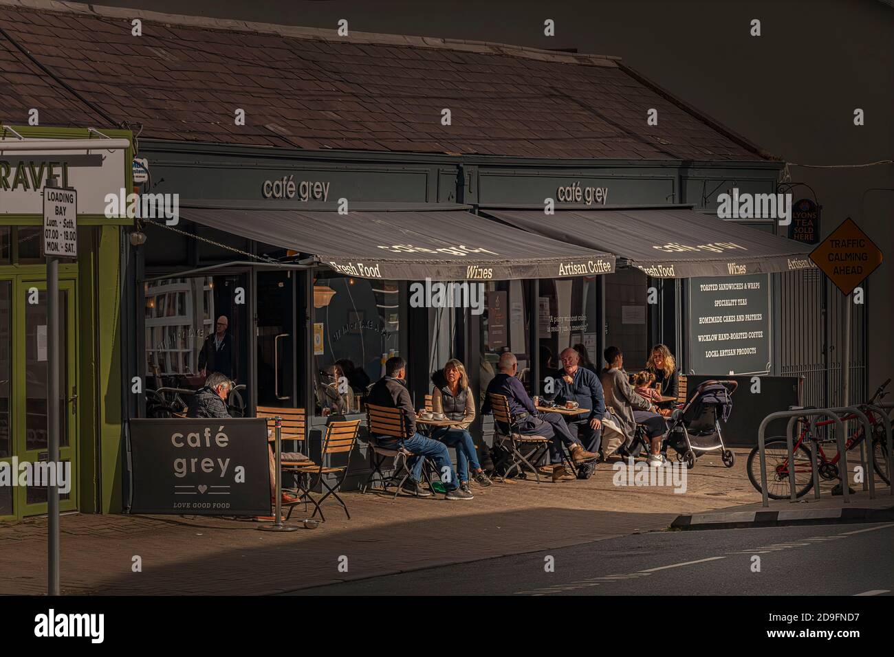 La vie quotidienne. Les gens assis dans un café en plein air et ayant un café à main Street, Greystones, Irlande. Banque D'Images