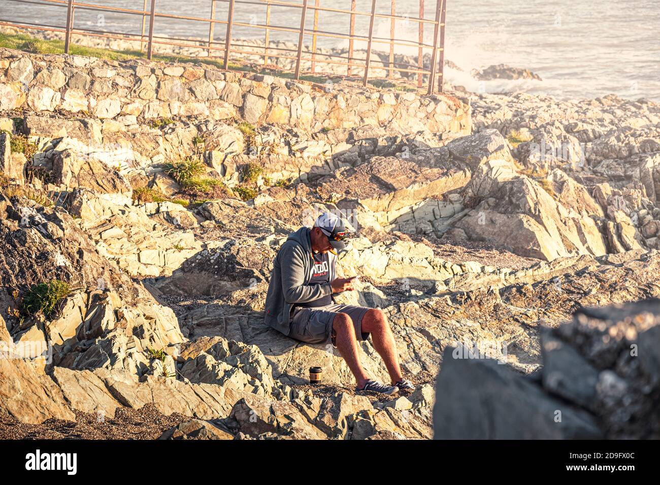La vie quotidienne. Homme avec téléphone portable assis sur des rochers près de la mer. Banque D'Images