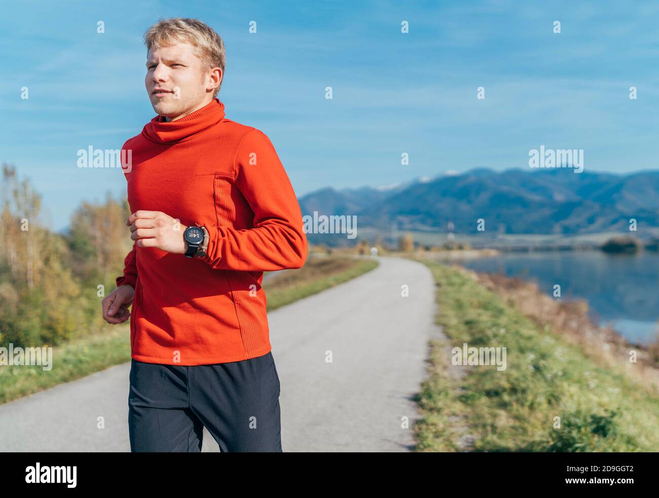 Un homme vêtu d'une chemise à manches longues rouge fait un jogging matinal sur la route avec un fond de montagne. Des activités sportives et un style de vie sain Banque D'Images