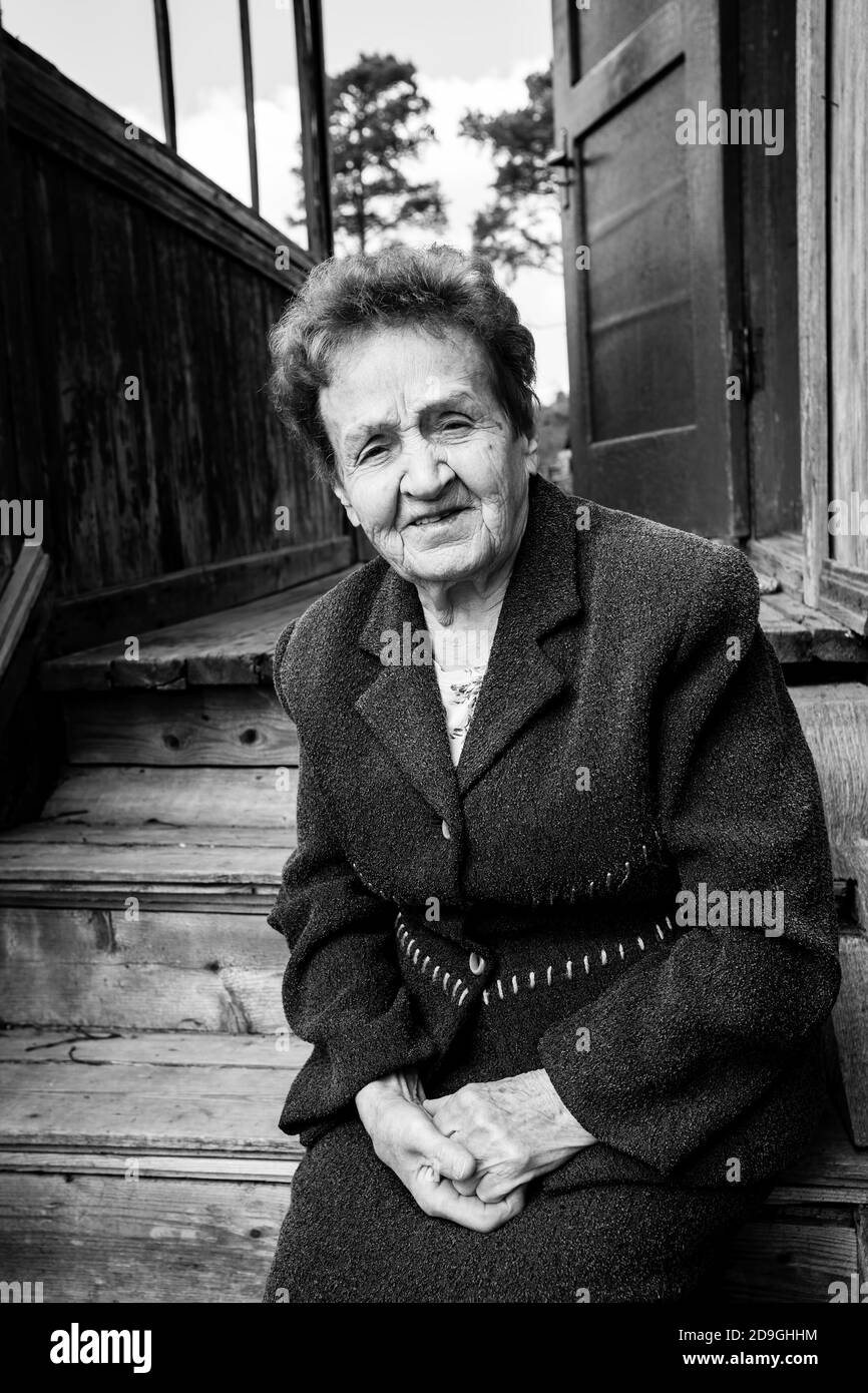 Une vieille femme assise sur le porche d'une maison rurale. Photographie en noir et blanc. Banque D'Images