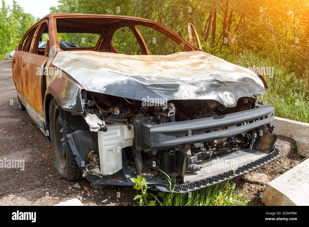 Vue de face d'une voiture de tourisme rouillée brûlée le jour de l'été, pare-chocs manquant, capot froissé. Banque D'Images