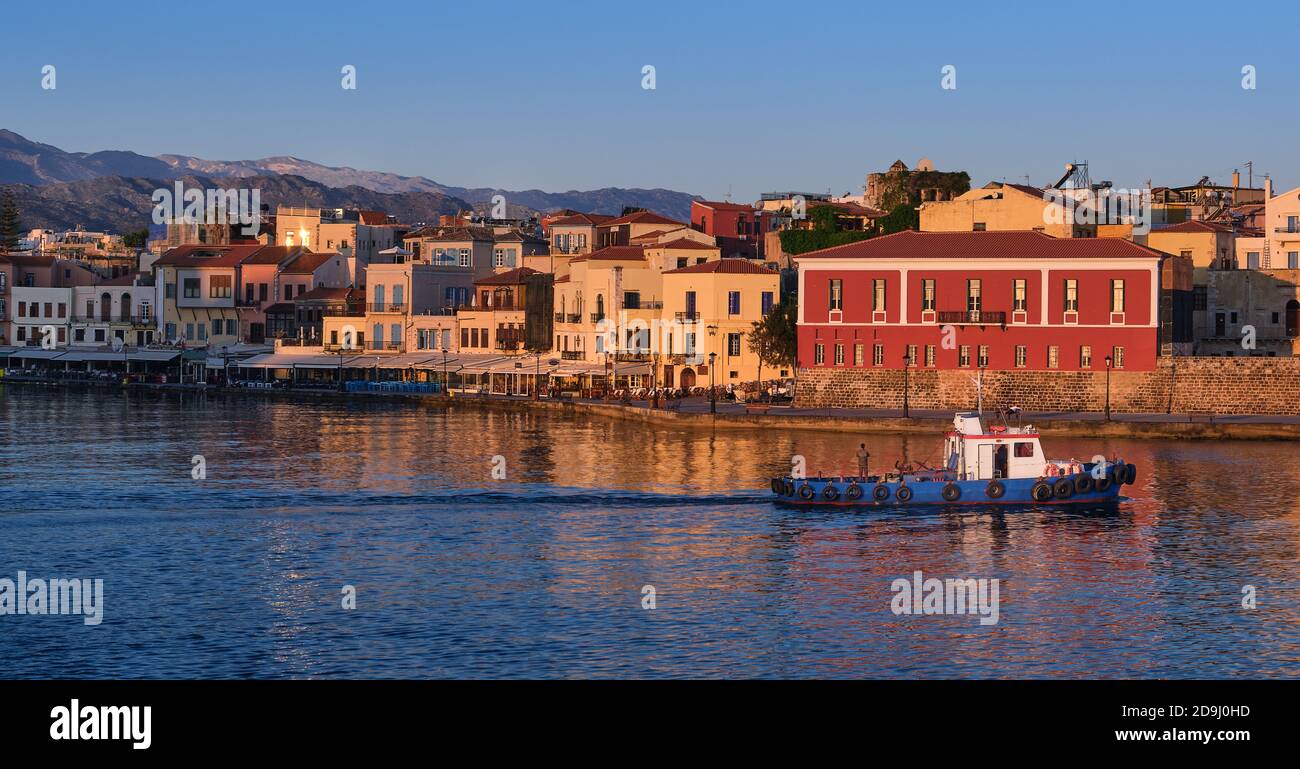 Bateau de pêche passe par le quai du vieux port vénitien, musée maritime de Crète à Chania, Crète, Grèce. Lever du soleil, collines et montagnes crétoises. Premiers rayons du soleil Banque D'Images