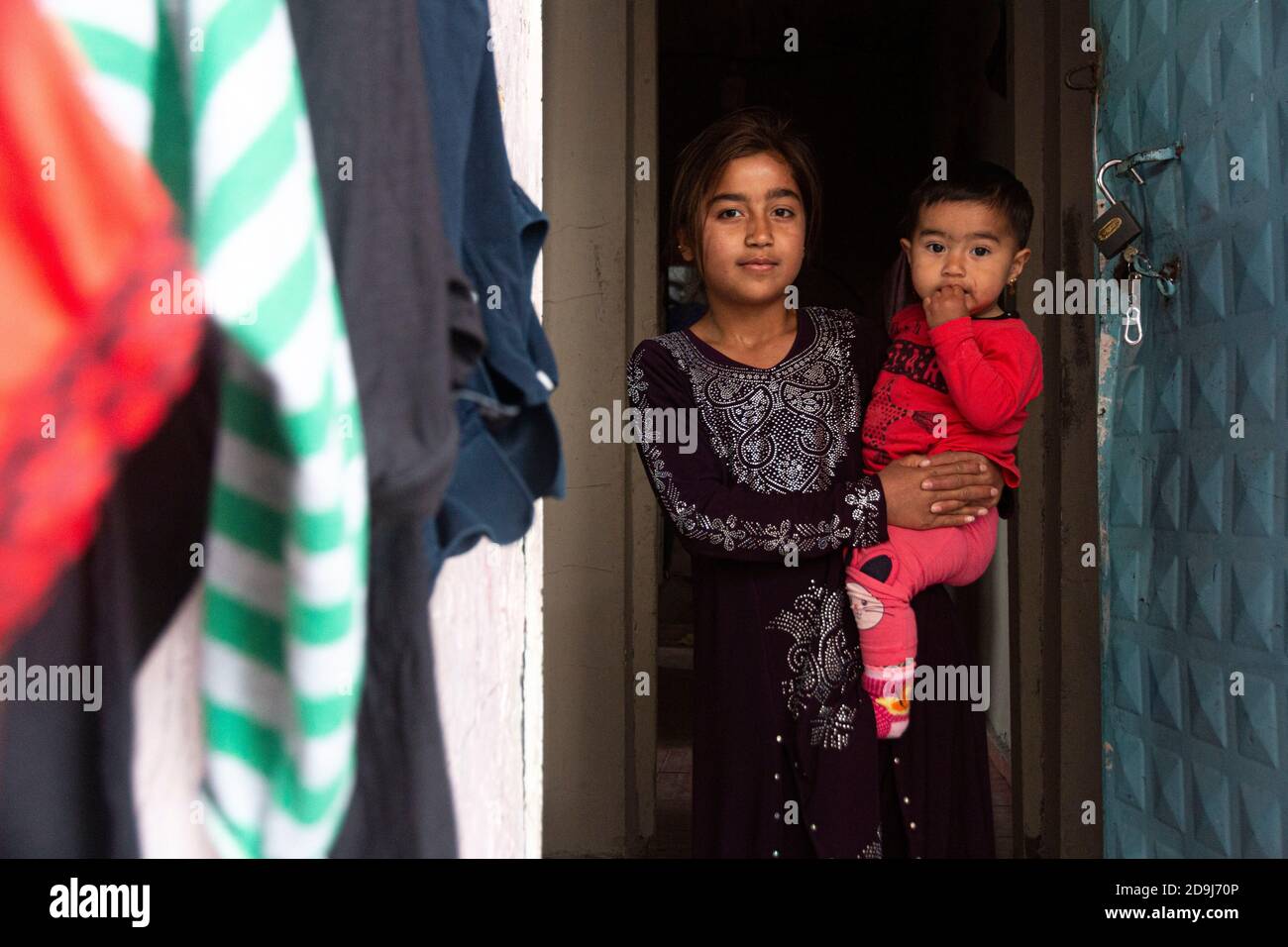 Une fille syrienne portant son frère pose une photo dans un camp de réfugiés.selon les 77 000 réfugiés syriens qui séjournent dans la capitale turque tentent de survivre à l'épidémie de COVID-19 à Ankara Ulus. Dans la course à la survie, les enfants des réfugiés passent également un grand test. Les enfants qui ne reçoivent pas l'éducation, la santé et les services de soins adéquats essaient d'être heureux avec tout ce qu'ils trouvent. Pour ces enfants qui font des fusils en bois et des boules de papier sont toujours inquiets de leur destin futur. Banque D'Images