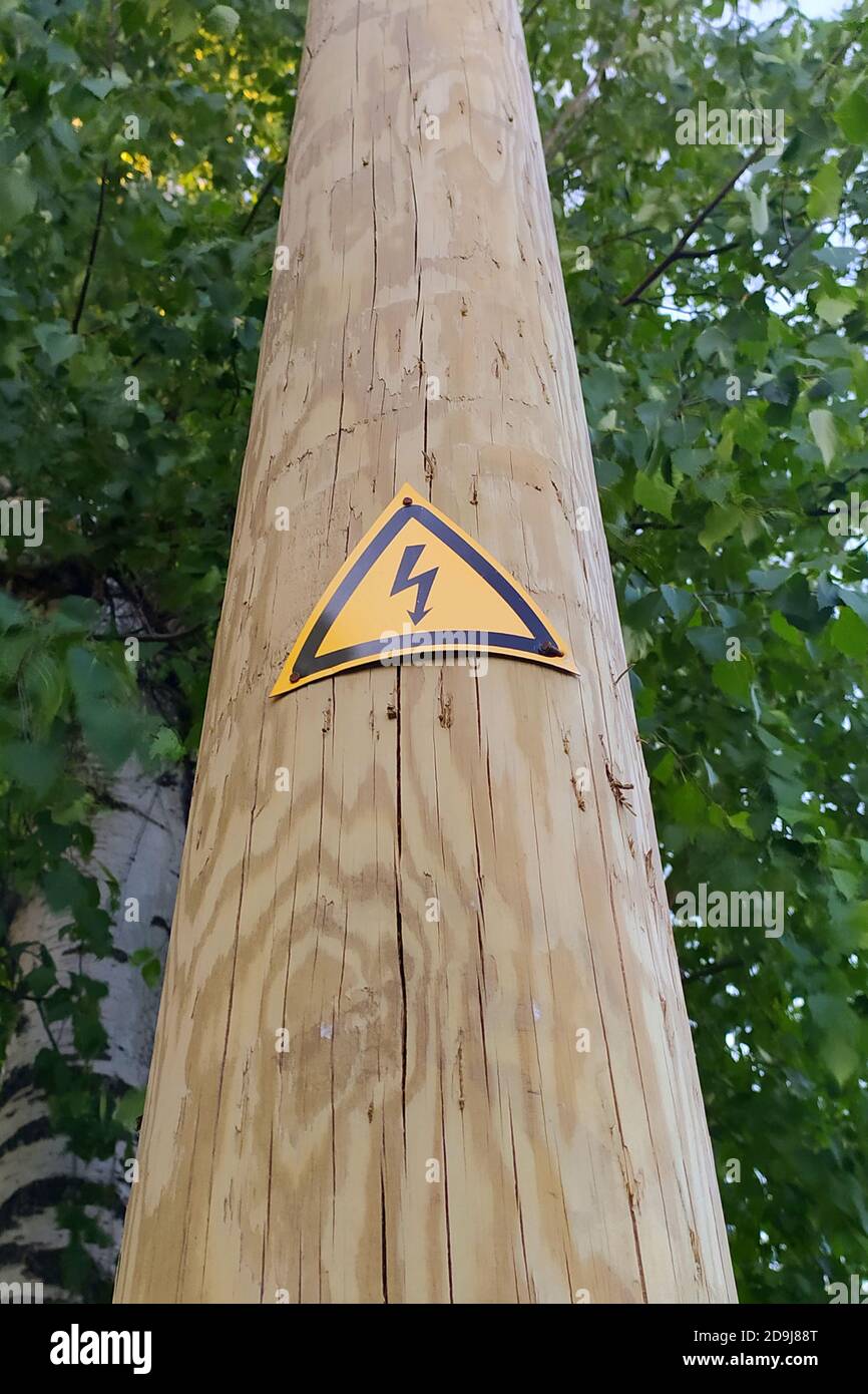 Signe de danger de choc électrique sur un poteau en bois. Éclair noir contre un triangle jaune. Photo avec espace vide pour le texte et le design. Banque D'Images