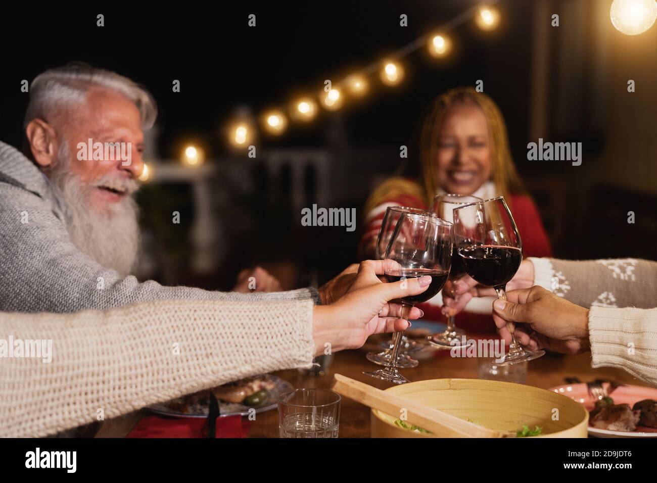 Heureux multiracial aînés de toaster avec des verres de vin rouge et de célébrer Vacances sur la maison patio dîner - personnes âgées style de vie concept Banque D'Images