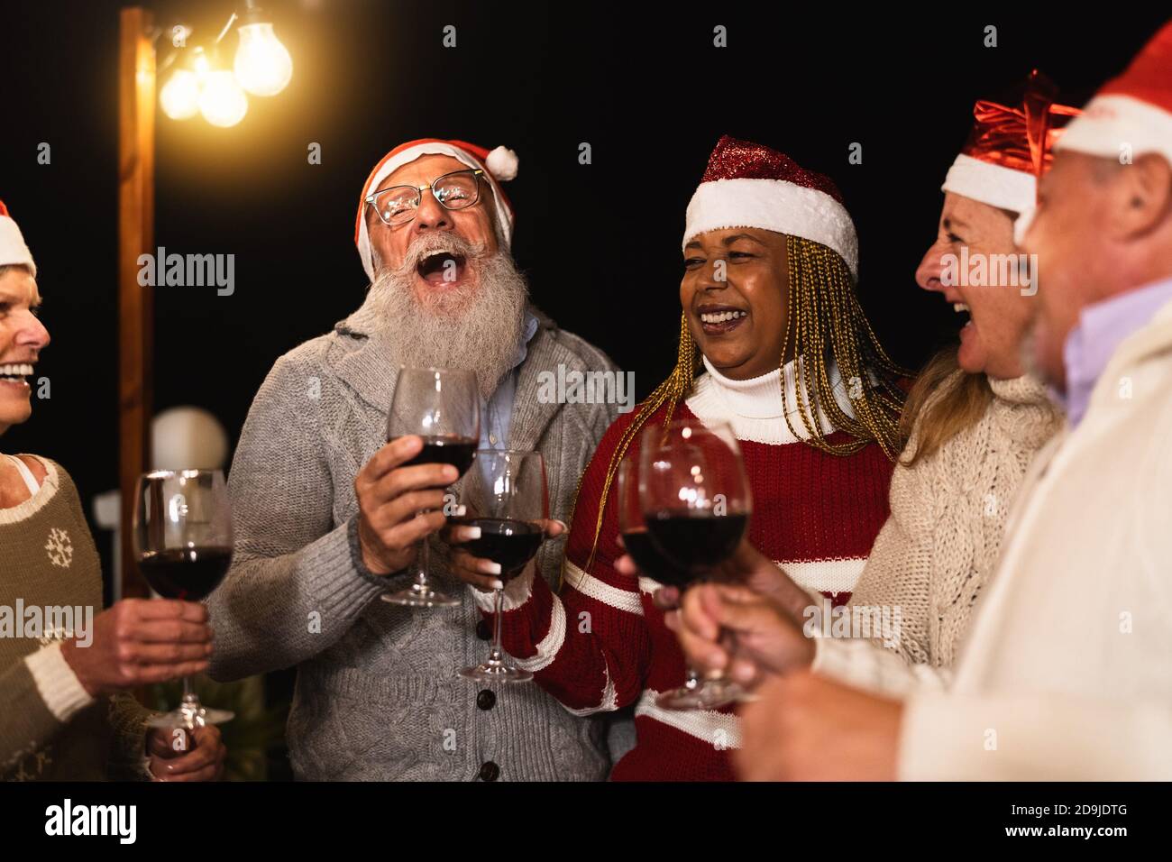 Heureux amis multiraciaux senior célébrant les vacances de Noël boire du vin rouge fête sur le patio de la maison Banque D'Images
