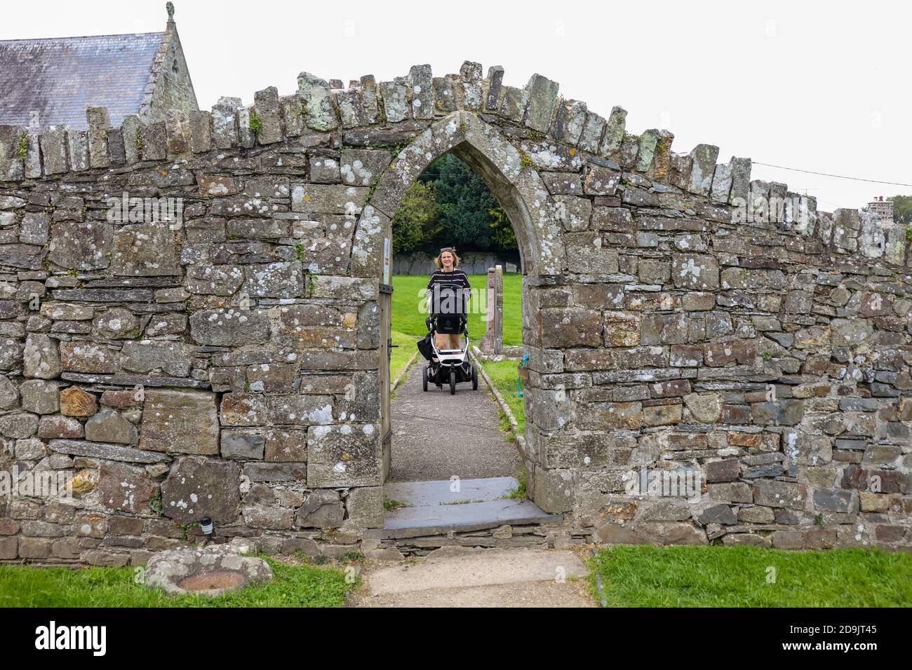 Maman avec bébé dans le pram traversant l'ancienne porte sur le mur entre le cimetière et l'abbaye de Saint-Dogmaels. Banque D'Images
