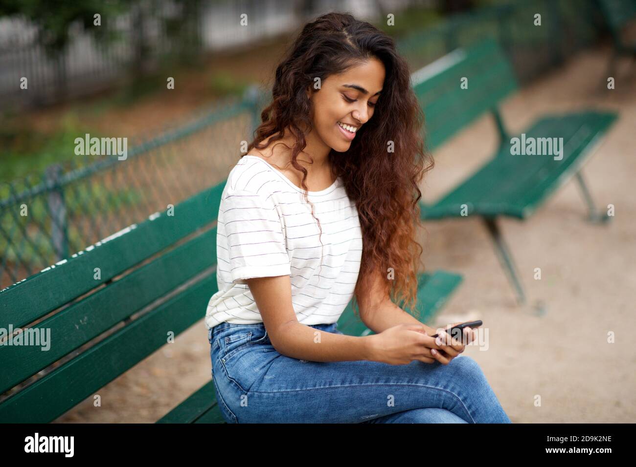Portrait latéral jeune femme indienne assise sur un banc de parc regardant au téléphone Banque D'Images