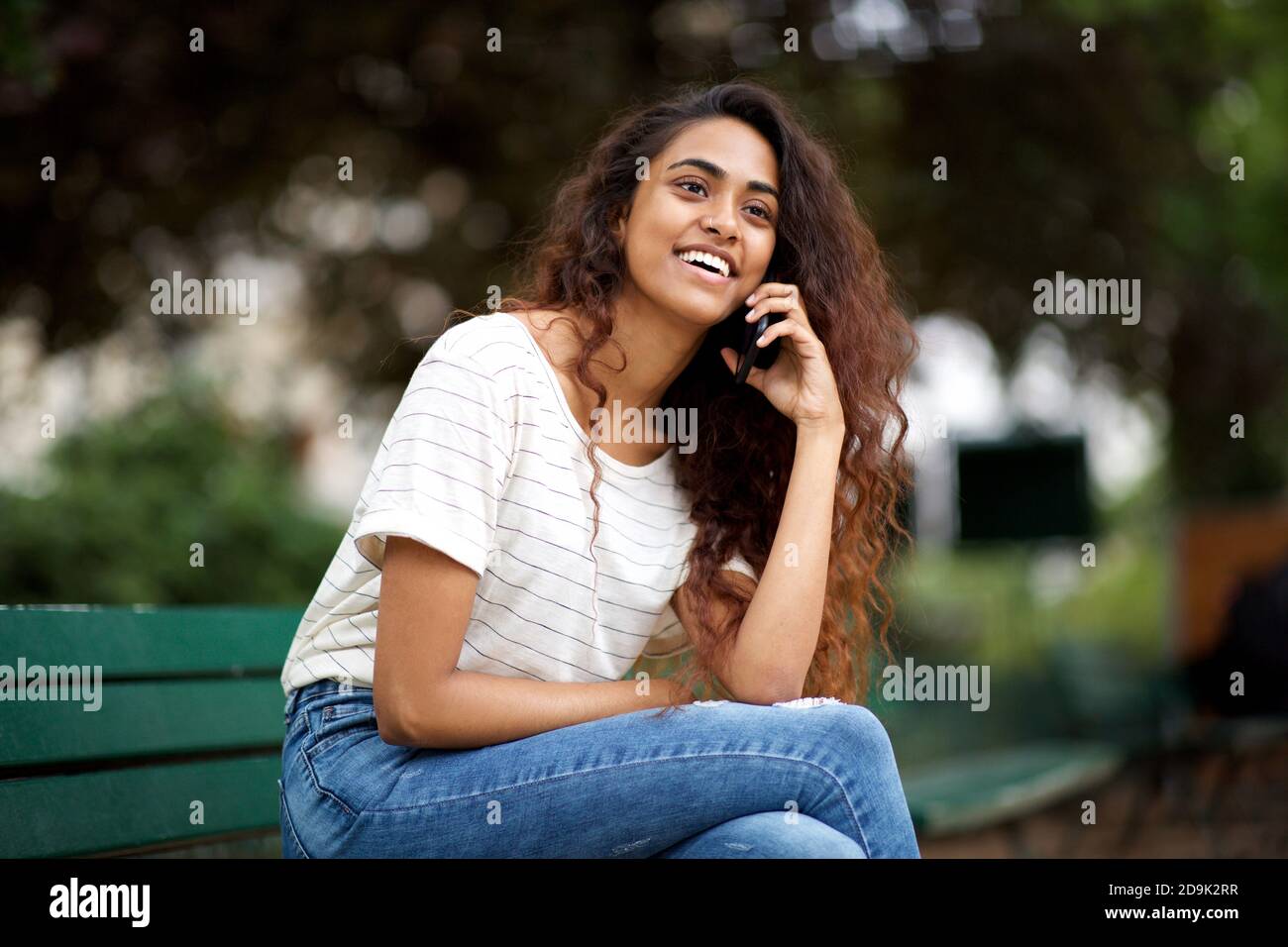 Portrait jeune femme indienne assise sur le banc du parc avec qui parler téléphone Banque D'Images