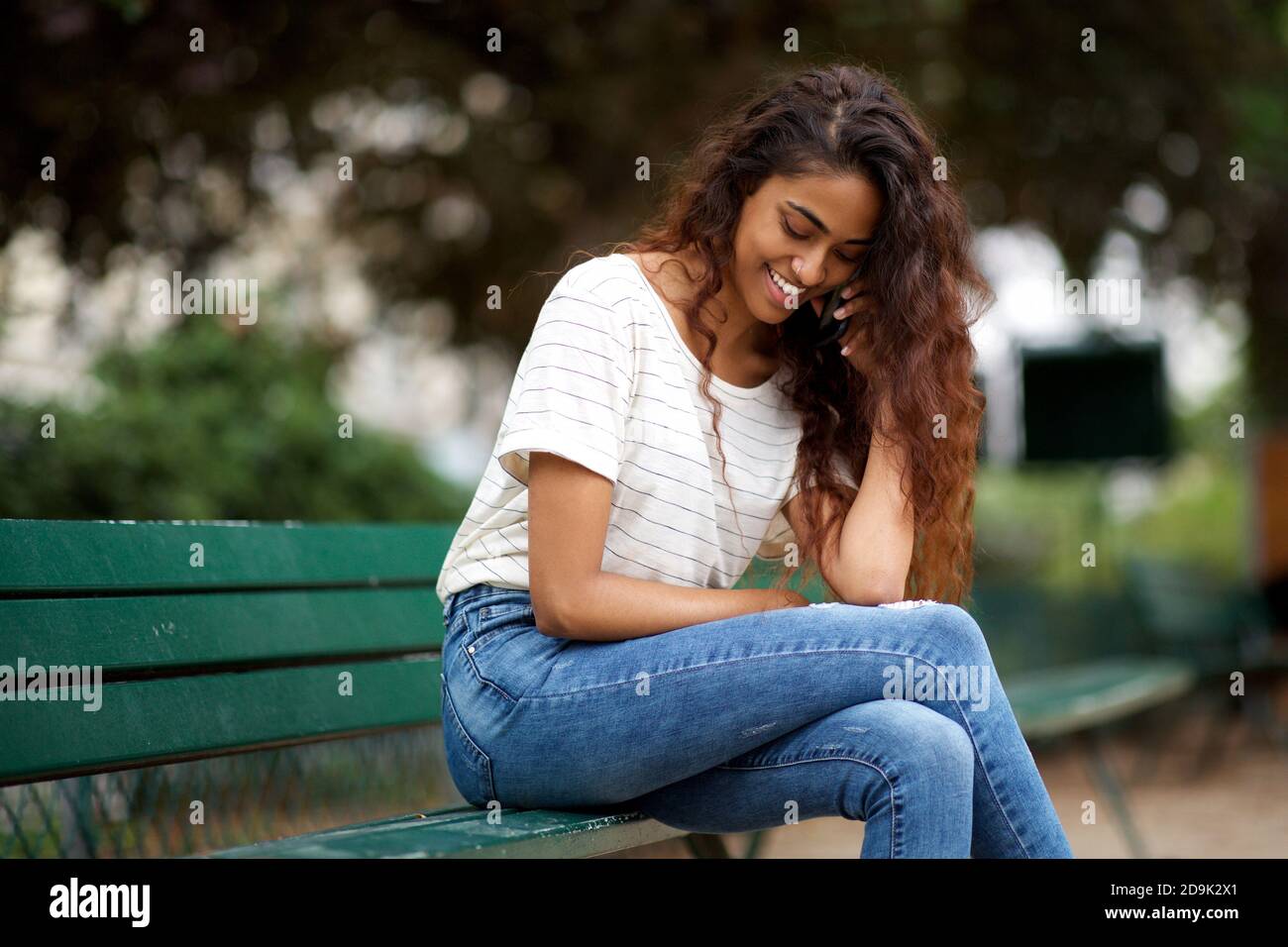 Portrait jeune femme indienne assise sur le banc du parc avec qui parler téléphone portable Banque D'Images