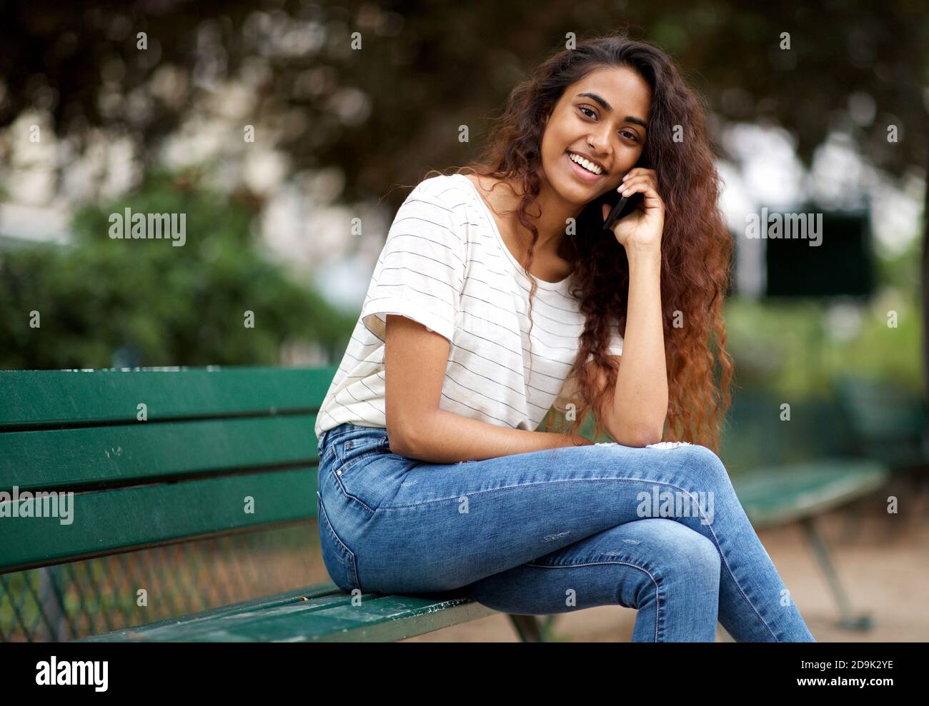 Portrait jeune femme indienne assise sur le banc du parc avec qui parler téléphone portable Banque D'Images