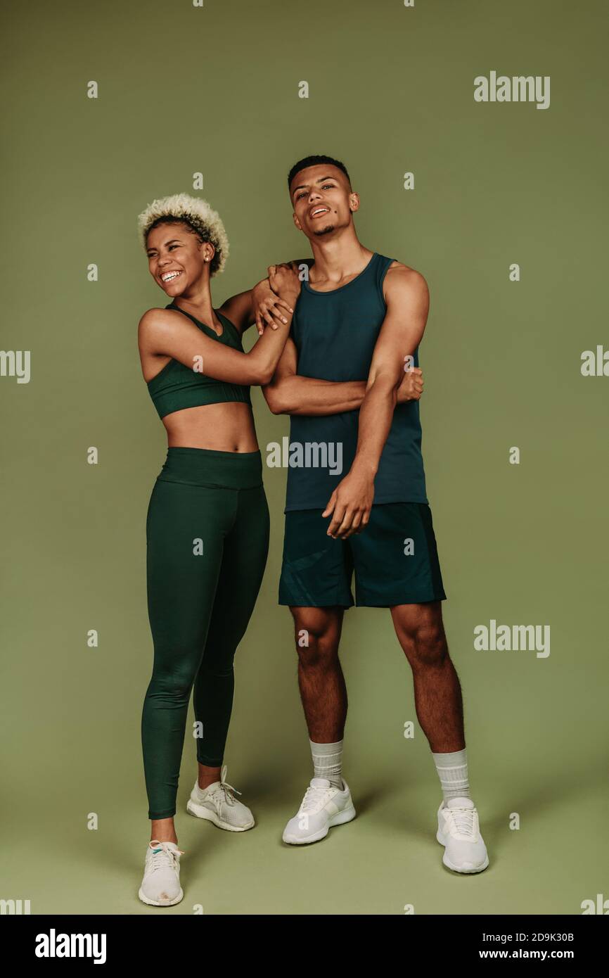 Couple en vêtements de fitness debout ensemble sur fond vert. Bonne forme physique femme debout avec un athlète masculin. Banque D'Images
