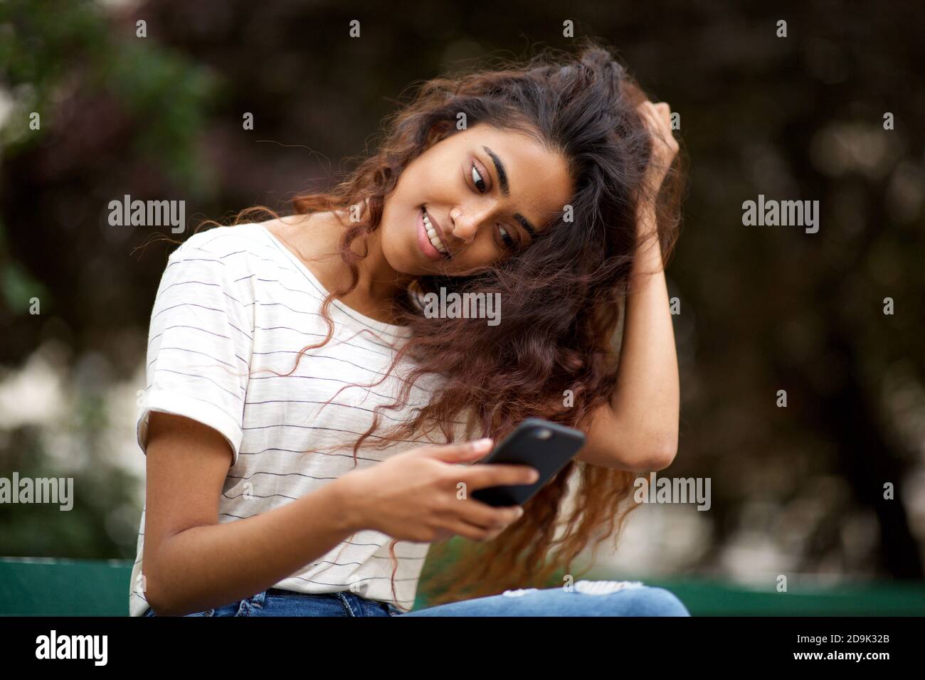 Gros plan portrait belle jeune femme indienne souriante dans le parc et regarder le téléphone Banque D'Images