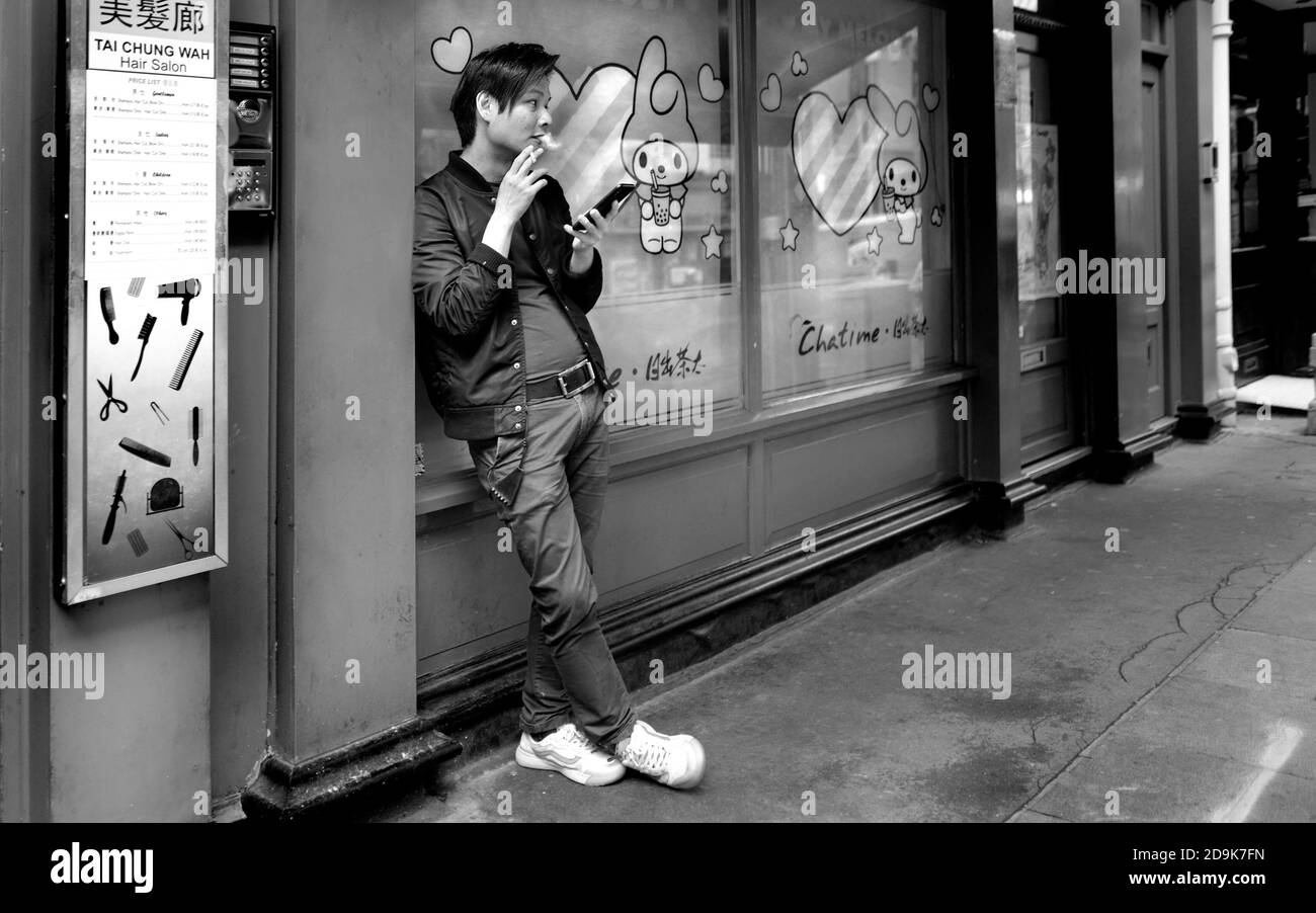 Londres, Angleterre, Royaume-Uni. Chinatown: Gerrard Street - jeune Chinois regardant son téléphone mobile et fume une cigarette Banque D'Images