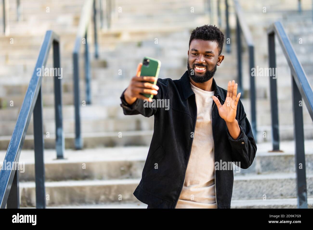 Un homme africain heureux ayant un appel vidéo tout en marchant dans le rue Banque D'Images