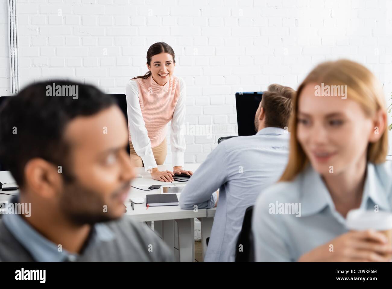 Femme d'affaires souriante regardant un collègue près d'un appareil dans un bureau Banque D'Images