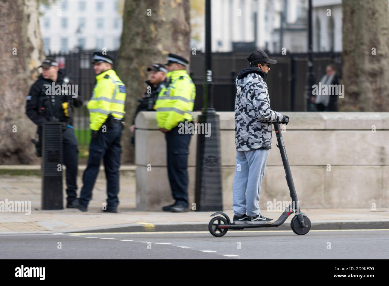 Jeune homme à bord d'un scooter électrique passé des policiers à Whitehall, Westminster, Londres, Royaume-Uni, Eco transport personnel illégalement monté sur la route Banque D'Images