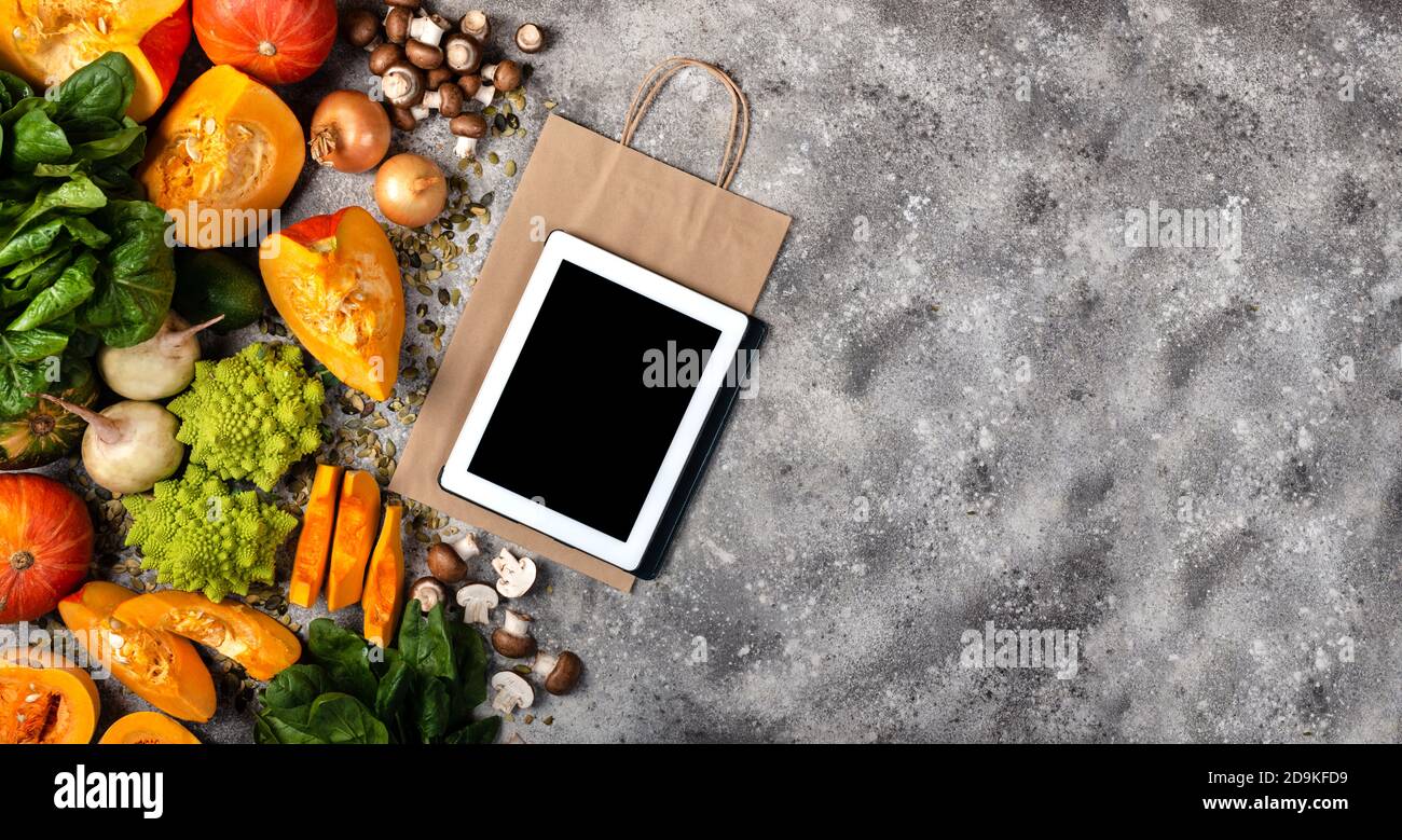 Concept d'épicerie en ligne. Ordinateur tablette et sac de papier avec des morceaux de citrouille différents légumes et verts. Bannière vue de dessus. Banque D'Images