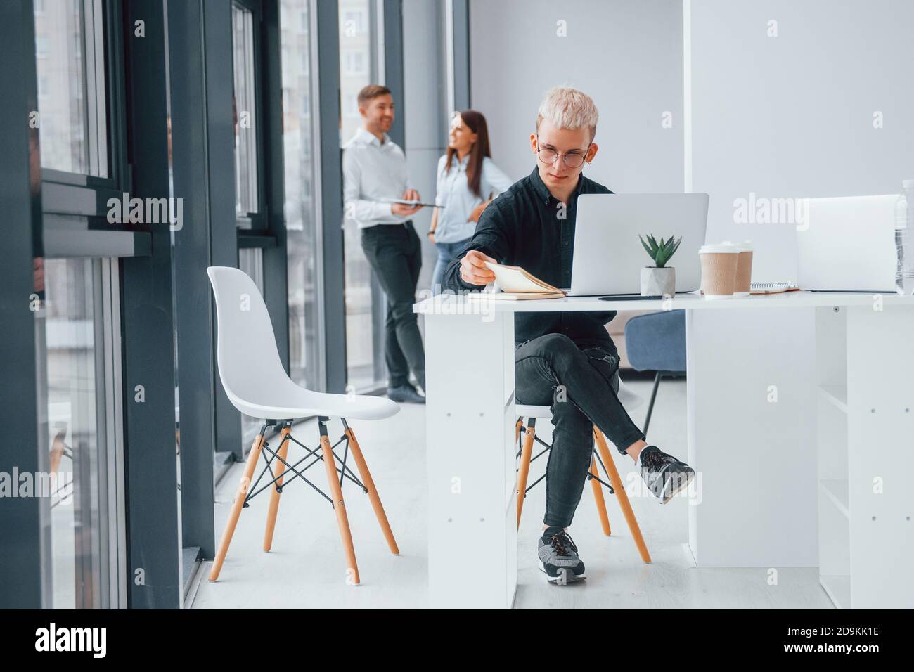 Taille basse avec ordinateur portable assis devant un groupe de jeunes une équipe réussie qui travaille par ordinateur portable et téléphone et de communiquer ensemble à l'intérieur dans le bureau Banque D'Images