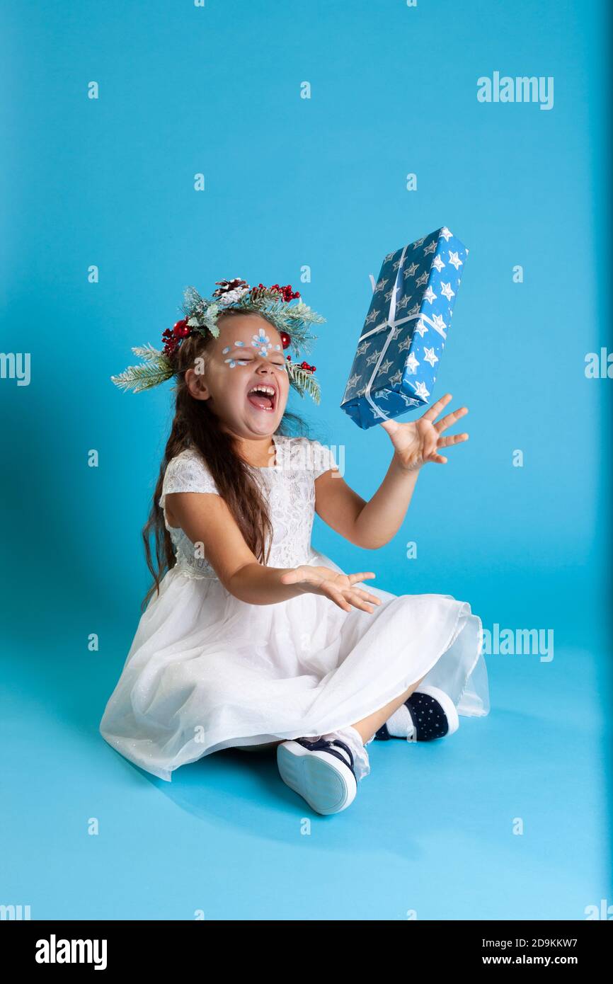 Une fille vêtue d'une robe princesse blanche, portant une couronne et des  baskets jette une boîte cadeau et rie avec bonheur, isolée sur un fond bleu  Photo Stock - Alamy