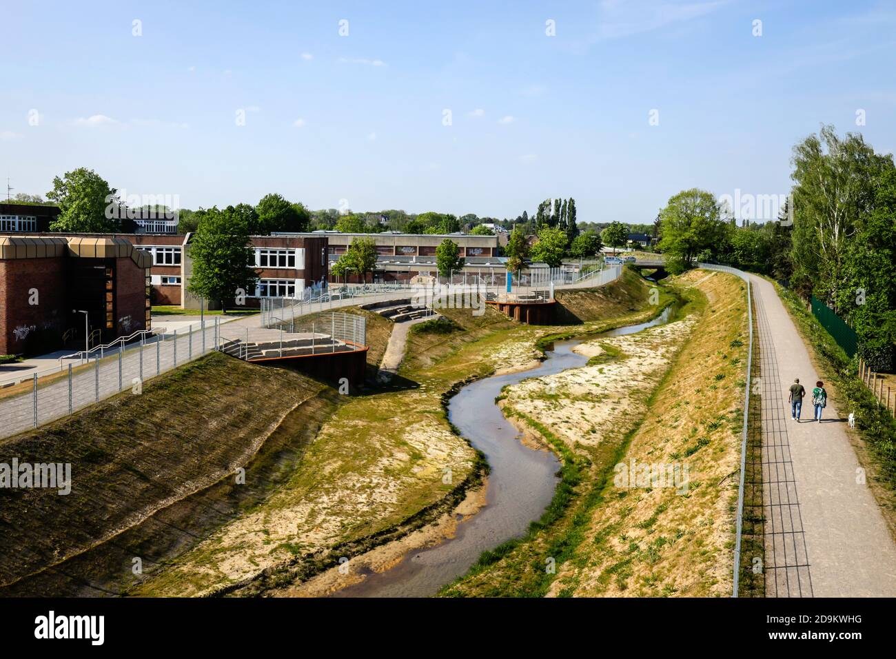 L'eau courante renatrée, le Hellbach appartient au système de l'Emscher, était auparavant un canal ouvert, au-dessus du sol des eaux usées, à gauche le Käthe-Kollwitz-Gesamtschule et la salle de classe bleue, à droite un nouveau sentier et sentier cyclable, conversion d'Emscher, Recklinghausen, région de Ruhr, Rhénanie-du-Nord-Westphalie, Allemagne Banque D'Images