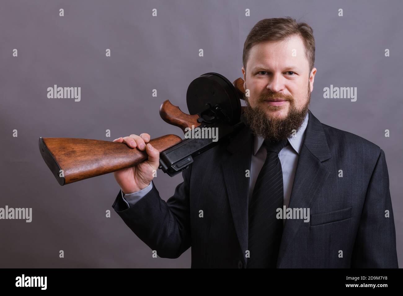 Homme mûr habillé en costume avec tommy Gun sur gris arrière-plan Banque D'Images