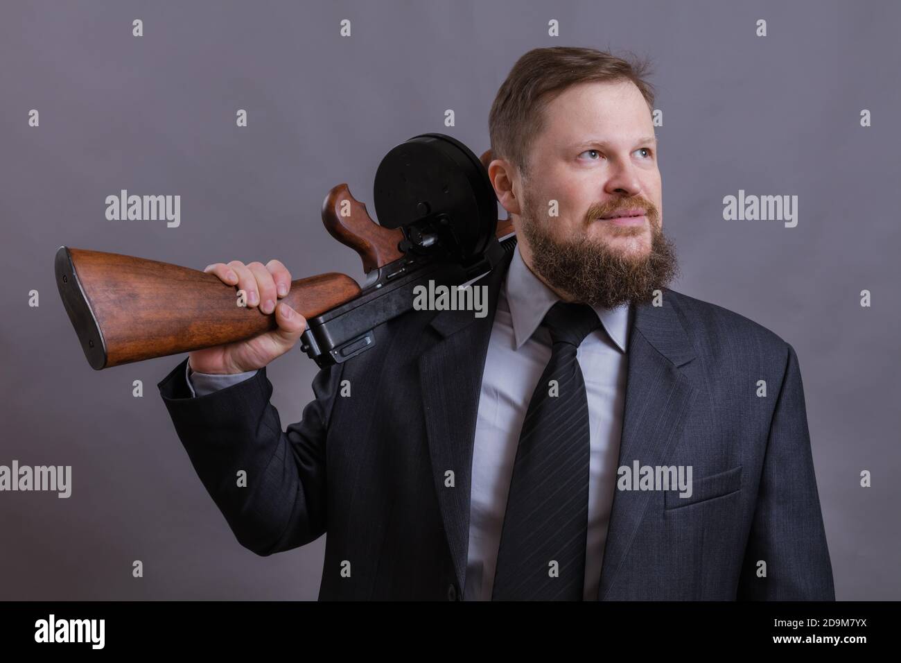 Homme mûr habillé en costume avec tommy Gun sur gris arrière-plan Banque D'Images