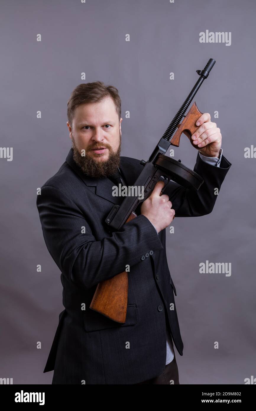 Homme mûr habillé en costume avec tommy Gun sur gris arrière-plan Banque D'Images