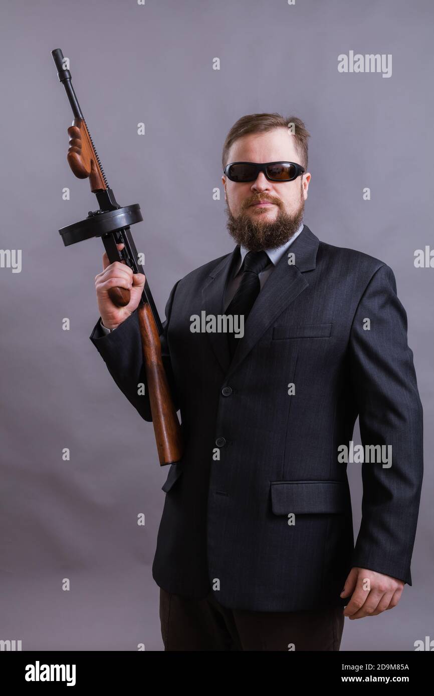 Homme à barbe mature en lunettes de soleil vêtu en costume avec tommy canon sur fond gris Banque D'Images