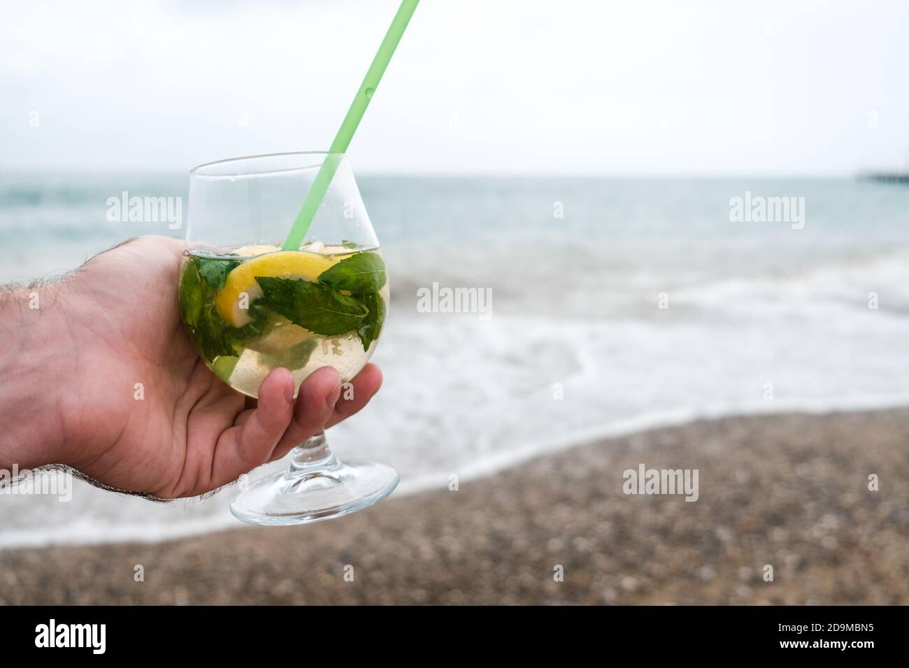 Main mâle blanche tenant un verre de vin avec un cocktail de mojito tropical. Escapade récréative ou vacances romantiques sur une île éloignée. Boisson de luxe sur la plage Banque D'Images