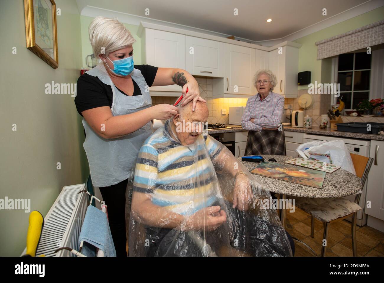 Homme âgé dans les années quatre-vingt ayant ses cheveux coupés par un coiffeur portant un EPI pour la protection contre le coronavirus tout en travaillant à distance, Angleterre, Royaume-Uni Banque D'Images