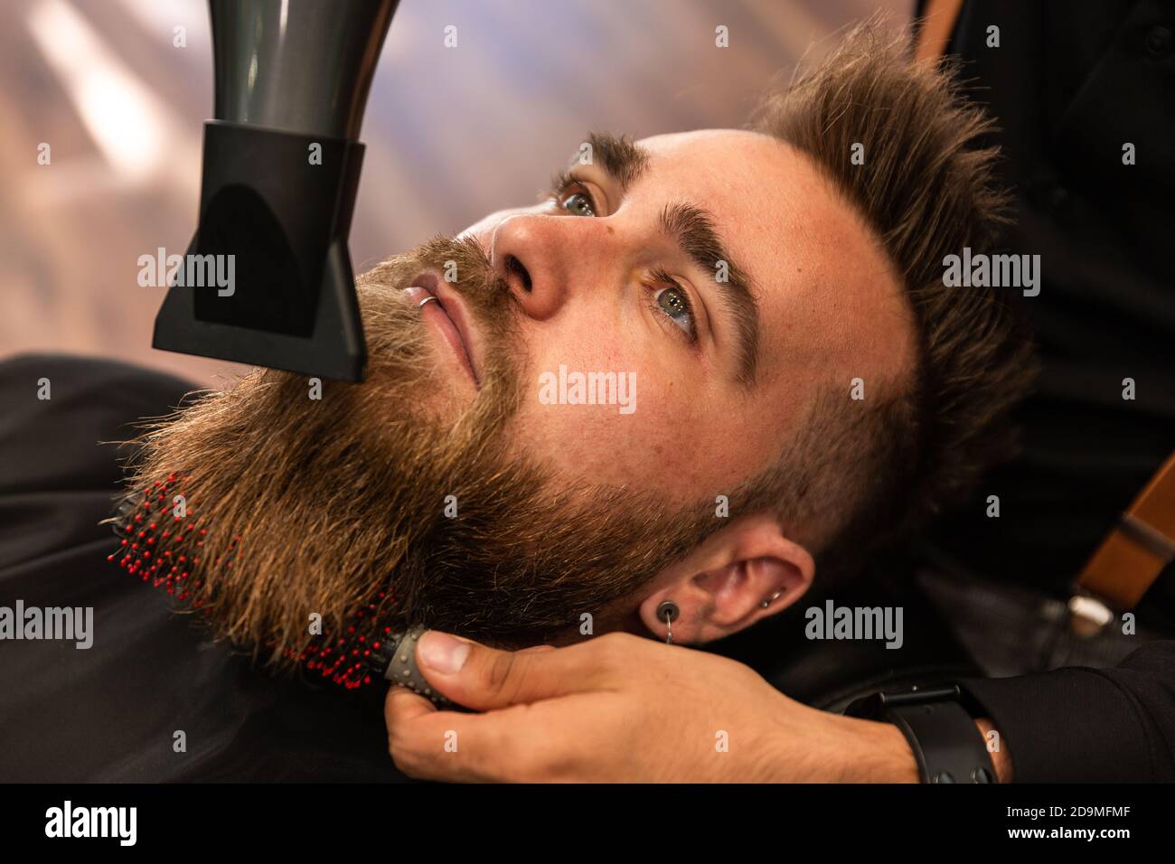 Un garçon caucasien avec une barbe est peigné par un coiffeur hispanique  dans le salon de coiffure avec un peigne et un sèche-cheveux. Zenithal  avion Photo Stock - Alamy