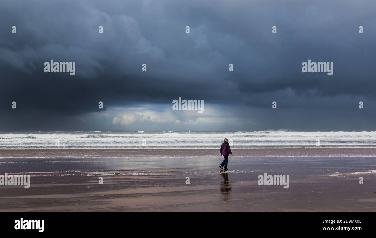 Une femme seule marchant le long du rivage sous un ciel orageux Banque D'Images