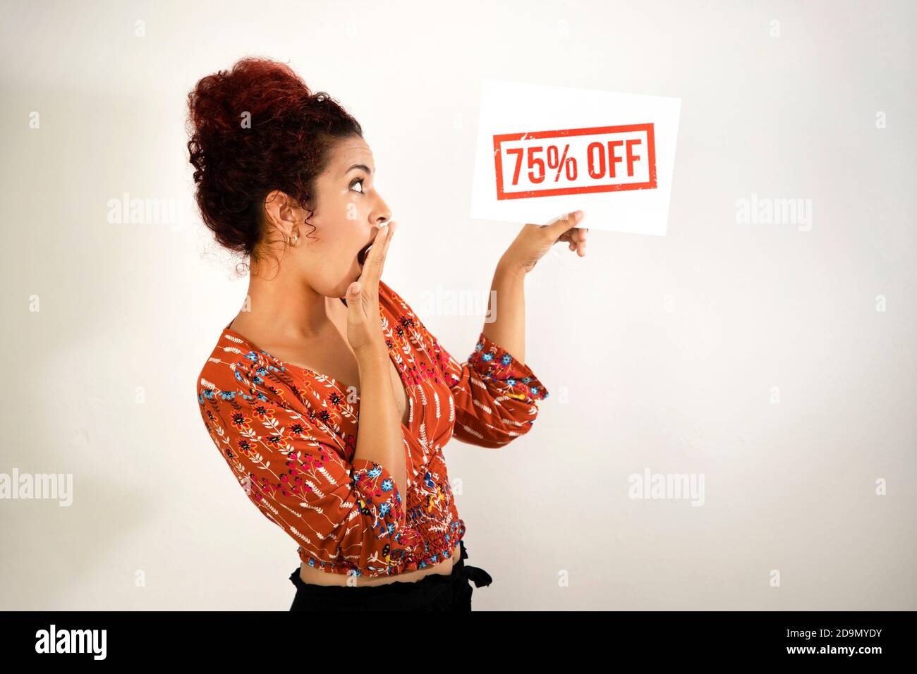 Très stupéfait fille couvrant sa bouche ouverte avec une main ou avec l'autre main tenant un signe d'escompte de 75%. Jeune femme à peau blanche et rouge bouclés Banque D'Images