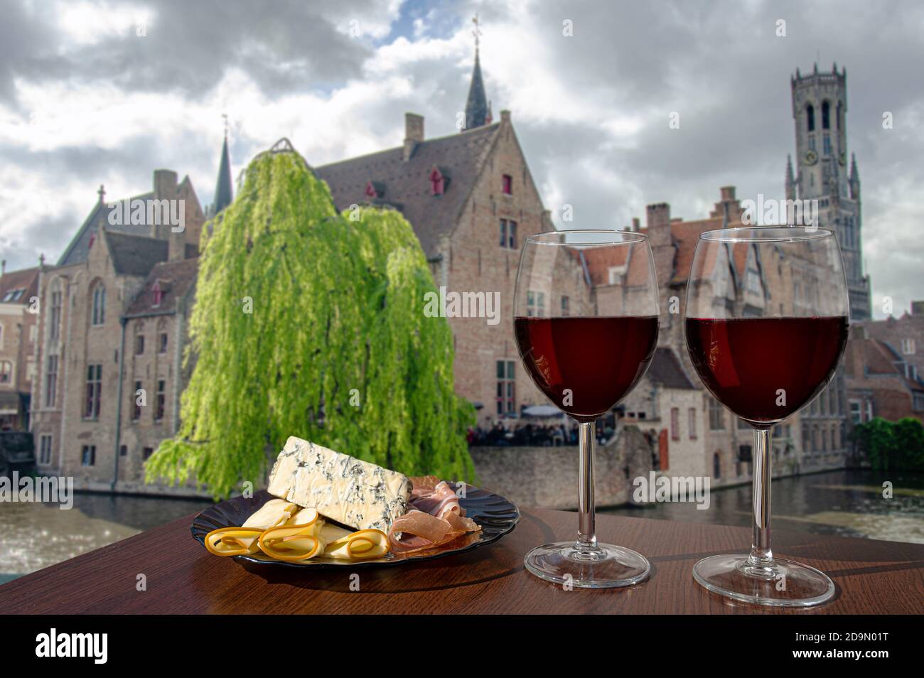 Deux verres de vin avec viande et fromage contre vue sur la vieille ville de Bruges et la tour du Beffroi à Bruges, Belgique. Verre de vin rouge avec différents en-cas Banque D'Images