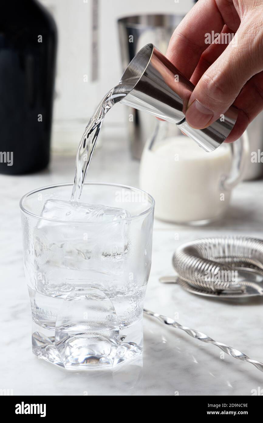 La main de l'homme verse de la vodka d'un puzzle dans un verre avec de la glace. Préparation de cocktails russes blancs Banque D'Images