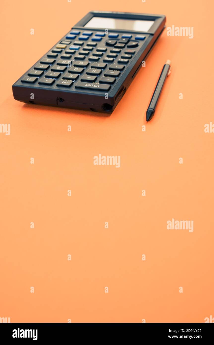 Un gros plan à faible angle d'une calculatrice graphique et d'un stylo minuscule isolé sur fond orange Banque D'Images