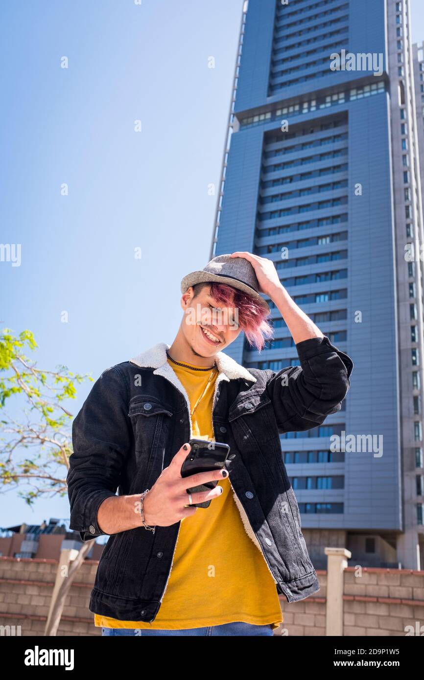 Gai alternative jeune homme adolescent utiliser le téléphone cellulaire pour écrire - bâtiment d'horizon dans le fond de la ville - concept de véritable jeune teeanger style de vie et dispositif de connexion - violet diversité cheveux et vêtements Banque D'Images