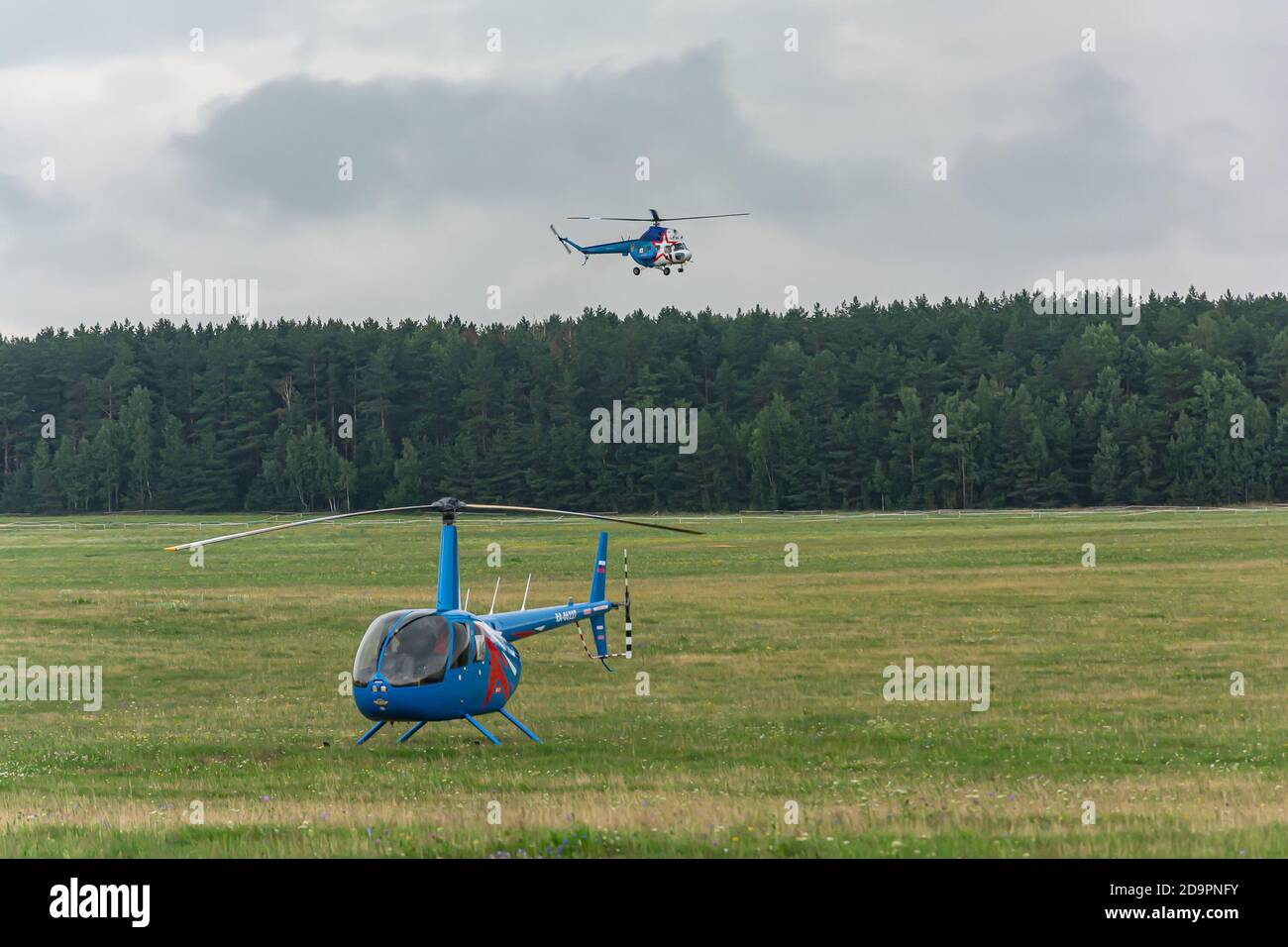 Bélarus, Minsk - 07/25/2018: L'hélicoptère est sur le champ de l'aérodrome et le deuxième hélicoptère arrive pour atterrir. Photos Banque D'Images