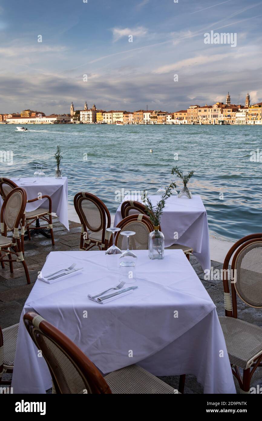 Table posée dans un restaurant à côté du canal Giudecca donnant sur les bâtiments éclairés de Venise, en Italie. Pris pendant la pandémie de Covid-19 Banque D'Images