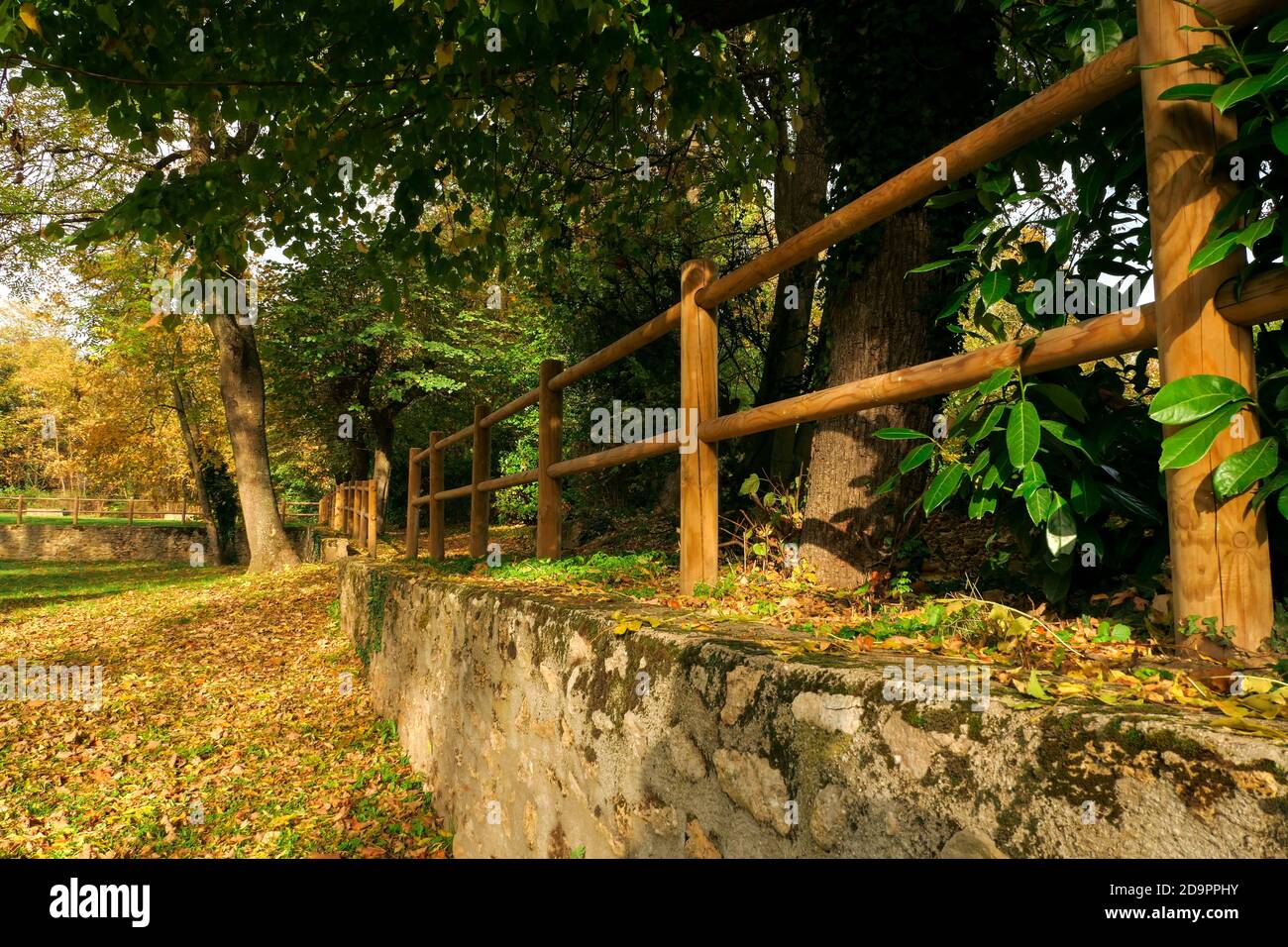 Mur de pierre en perspective dans un parc avec des clôtures en bois au sommet. Végétation et arbres en arrière-plan. Banque D'Images