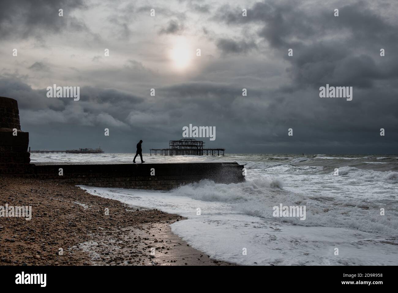 Un homme qui marche sur groyne à Brighton pendant un temps houleux, au Royaume-Uni Banque D'Images