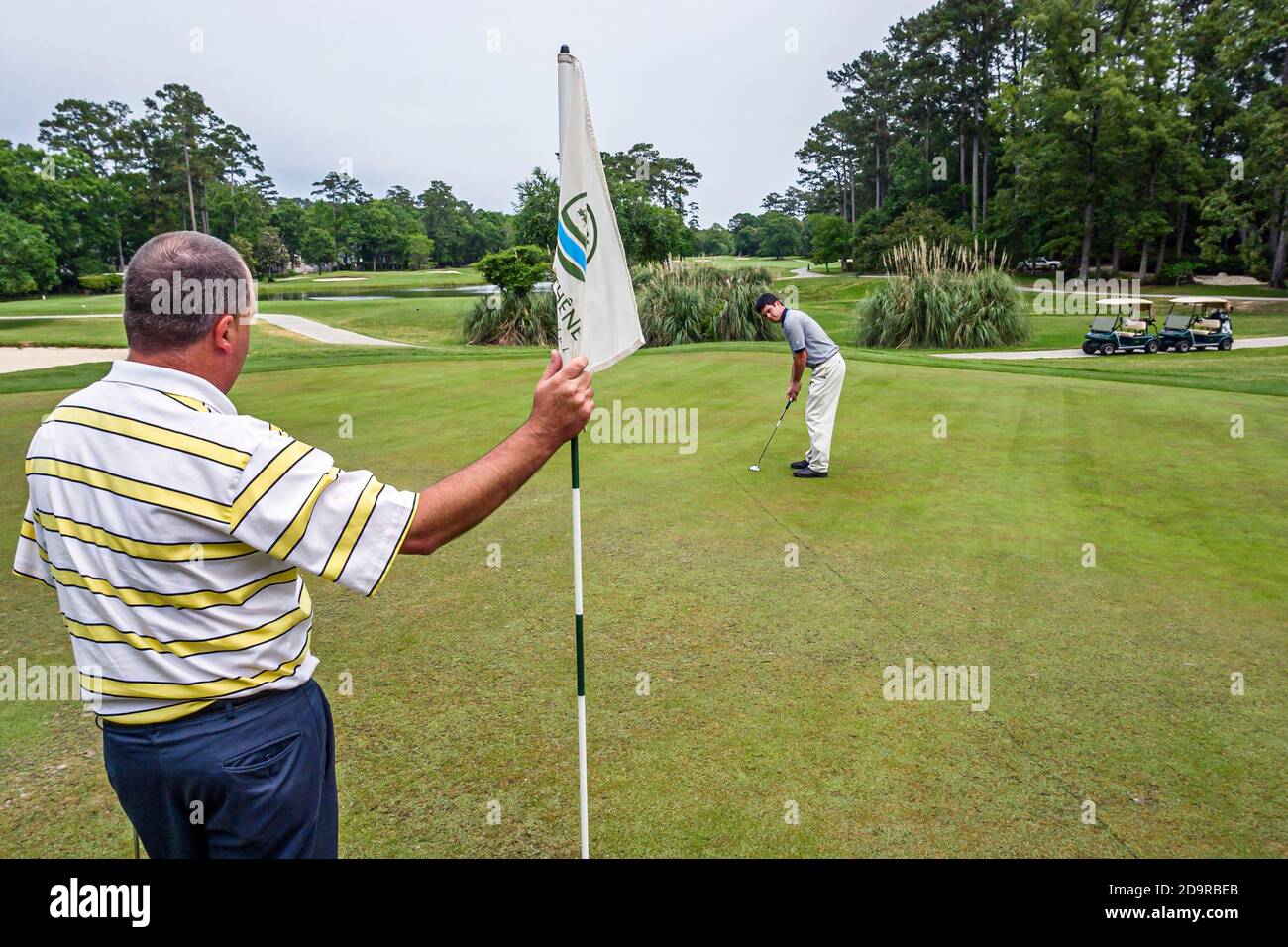 Louisiana Northshore,Mandeville,beau Chene Country Club golf parcours les golfeurs jouent à la mise verte, homme hommes amis tenant drapeau, Banque D'Images