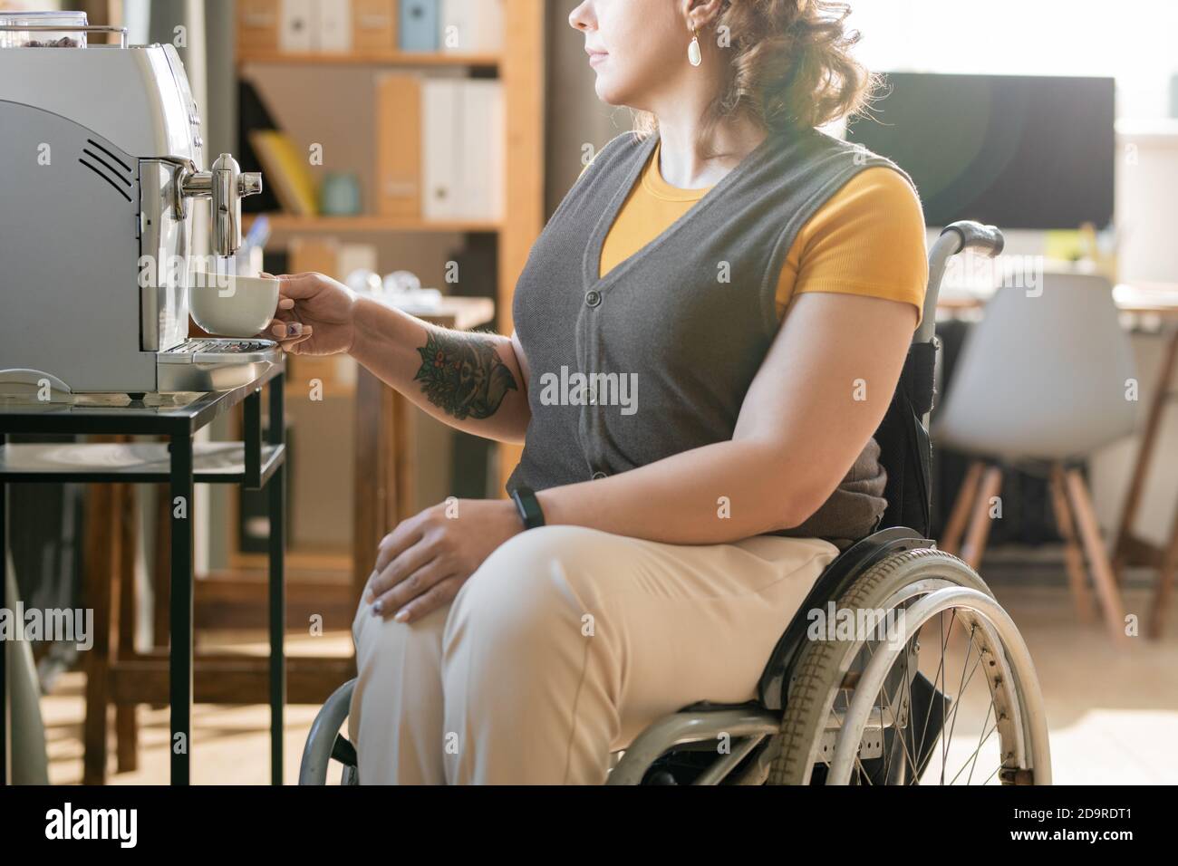 Une jeune femme d'affaires en fauteuil roulant prépare un café lors d'une pause au bureau environnement Banque D'Images