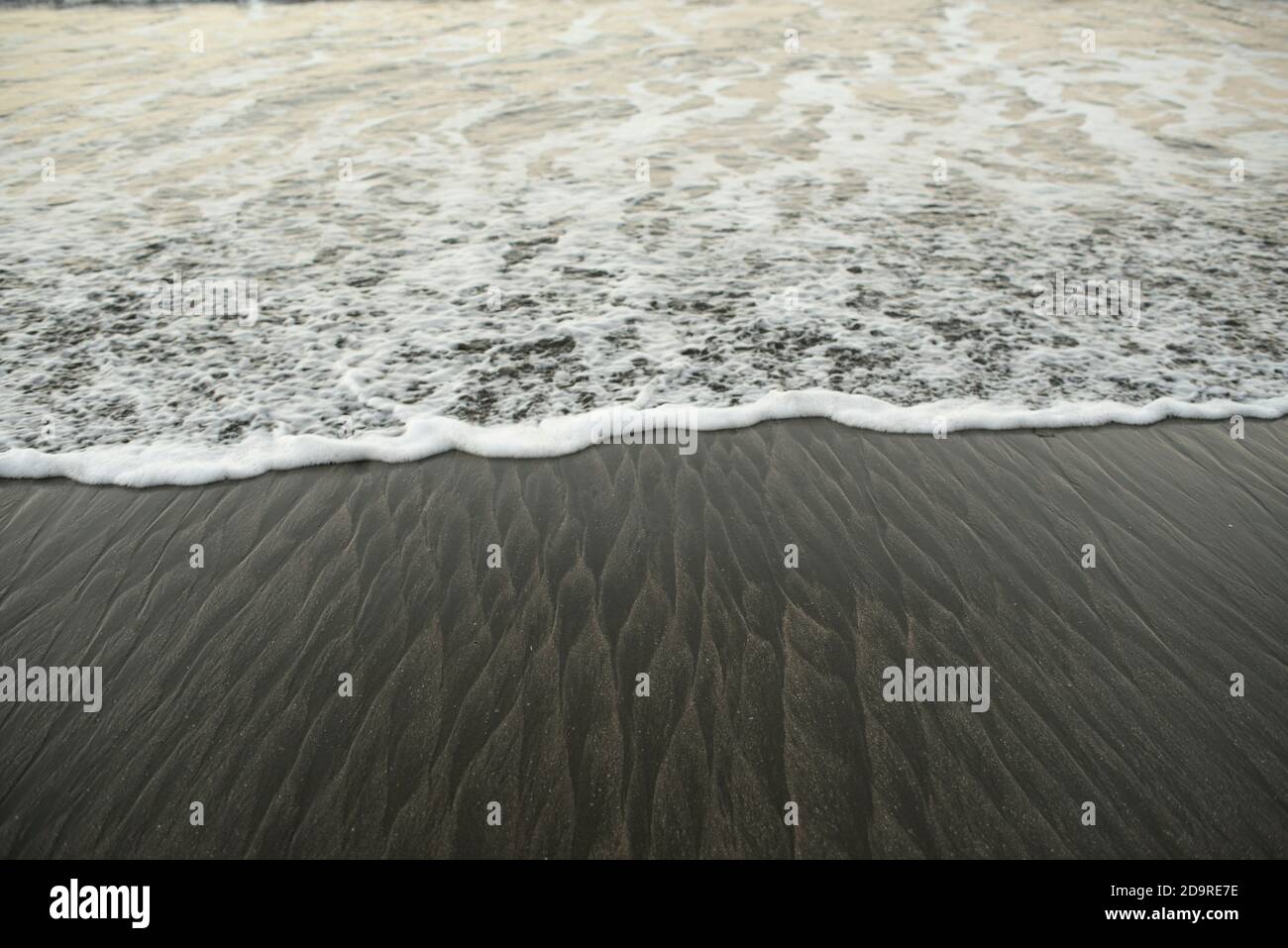 Gros plan de la vague océanique mousseuse qui atteint le rivage. Belle texture ondulée / motif sur sable noir. Santa Catalina, Panama, Amérique centrale Banque D'Images