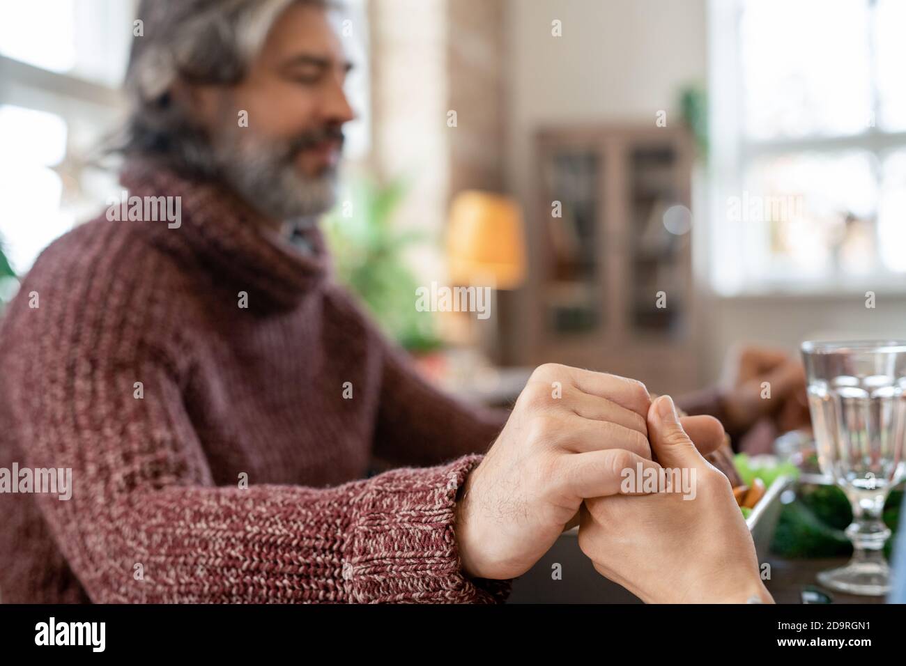 Mains de l'homme barbu mûr avec les yeux fermés et son femme priant avant le dîner Banque D'Images