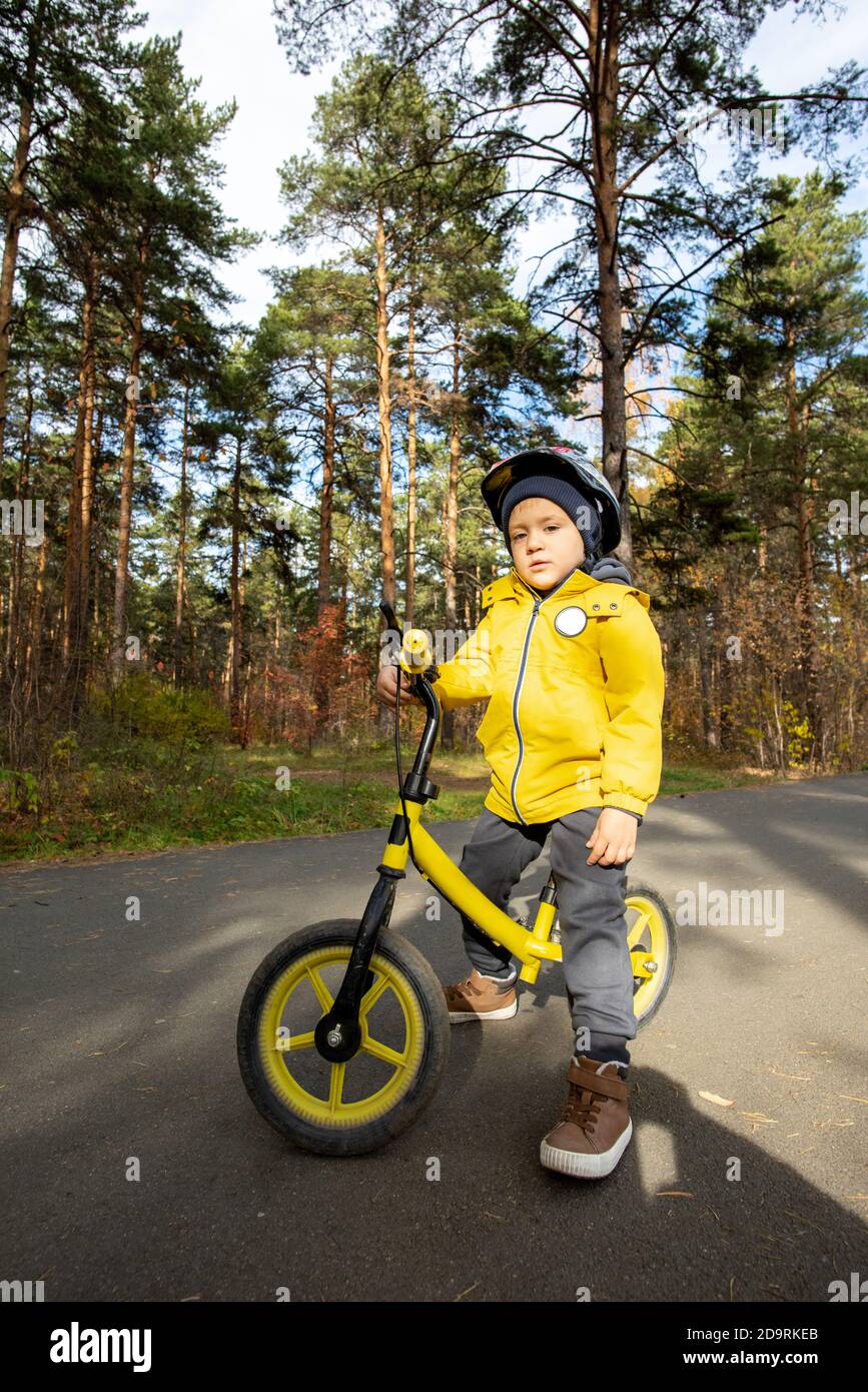 Adorable garçon en tenue décontractée et casque de protection debout près de lui equilibrer la moto Banque D'Images